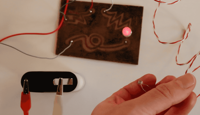 A white person's hand is playing with a light sensor that is attached to a PCB. When the light sensor is facing flight, an LED lights up.